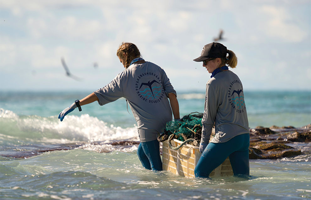 two environmentalists hold basket together wading in the ocean. 