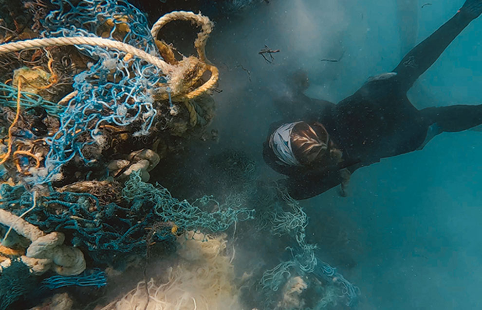 underwater shot of diver swimming towards colorful net full of various items. 