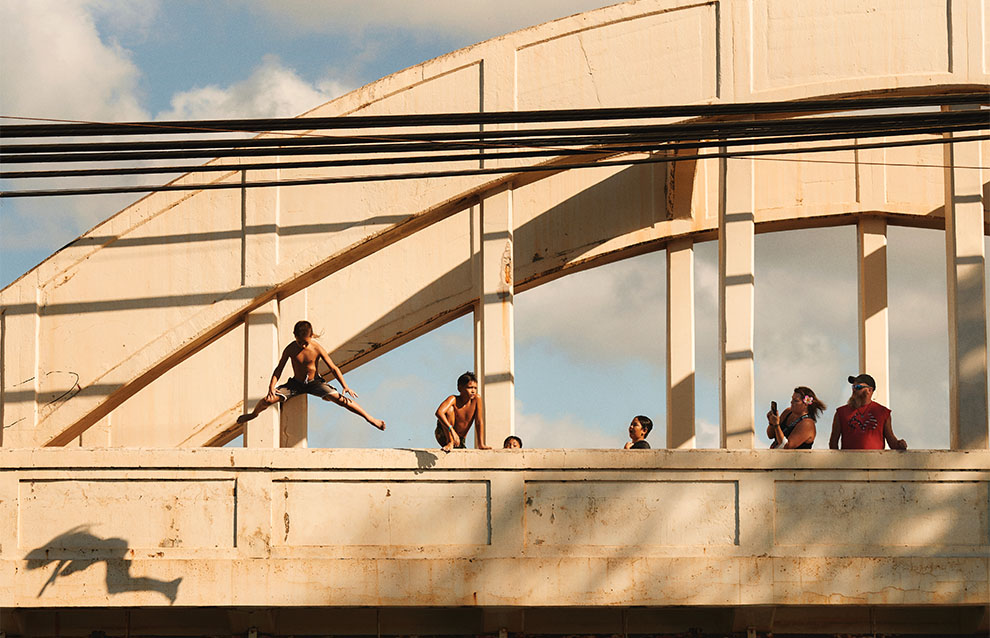 boy star jumps off bridge while friends watch on a warm day. 