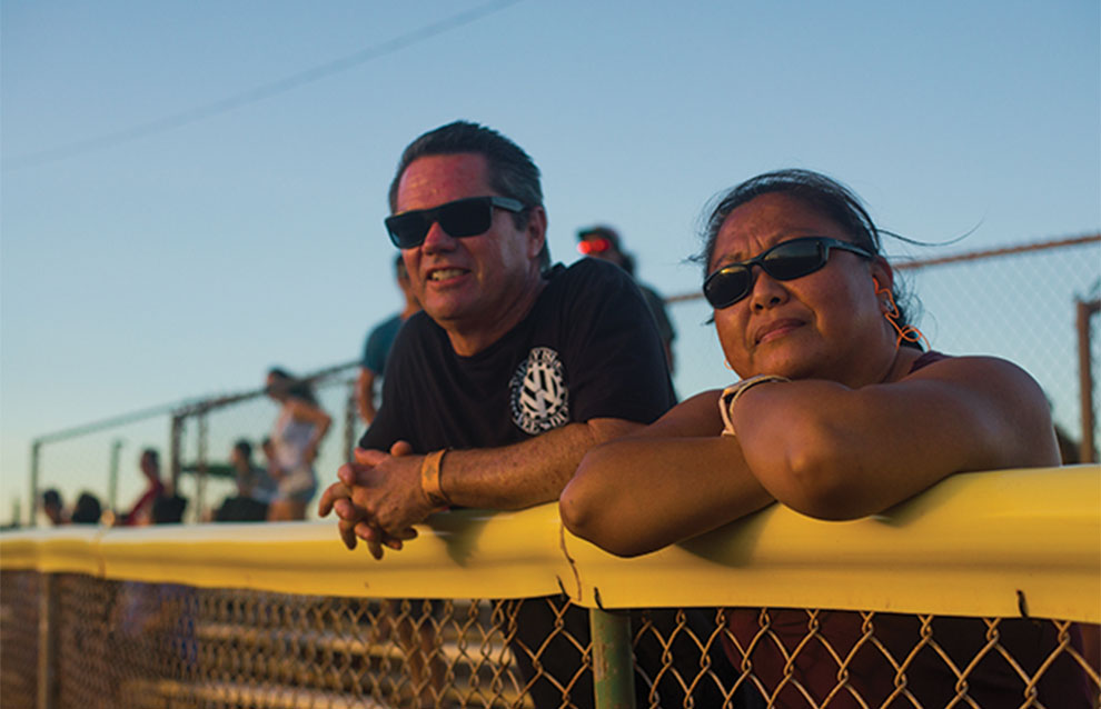 two people looking in the same direction holding onto top of wired fence against a blue sky