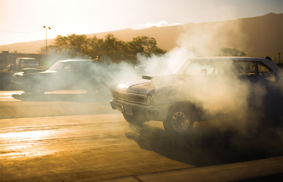 two race cars racing on a dusty road with a plume of smoke