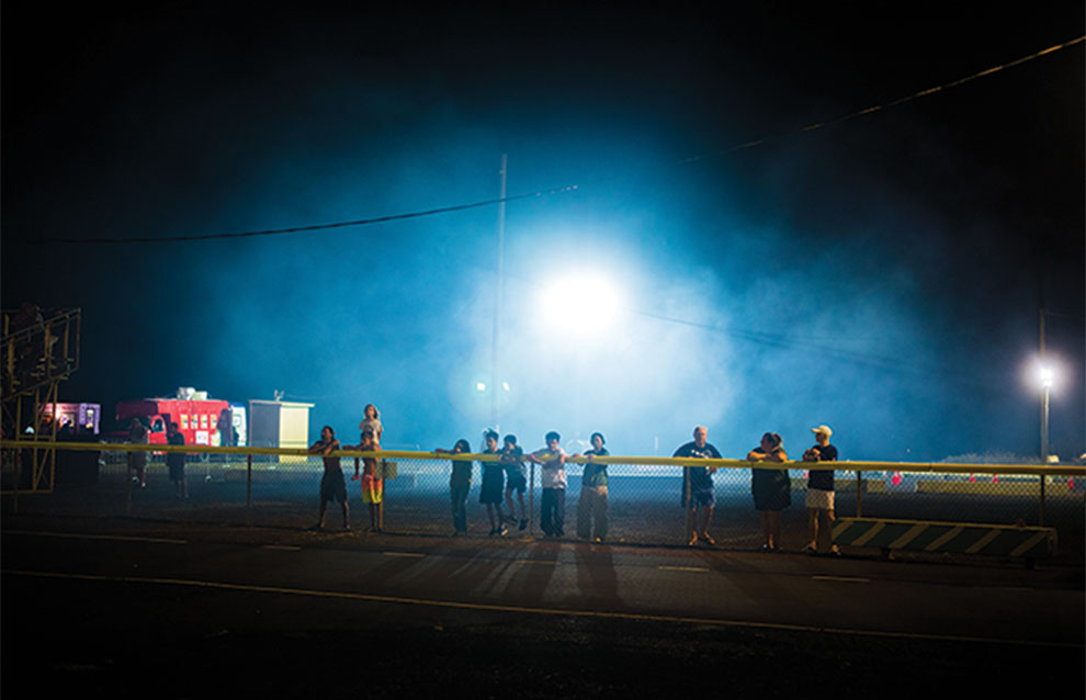 group of people at night in distance standing on race track with a blinding light casting over the center