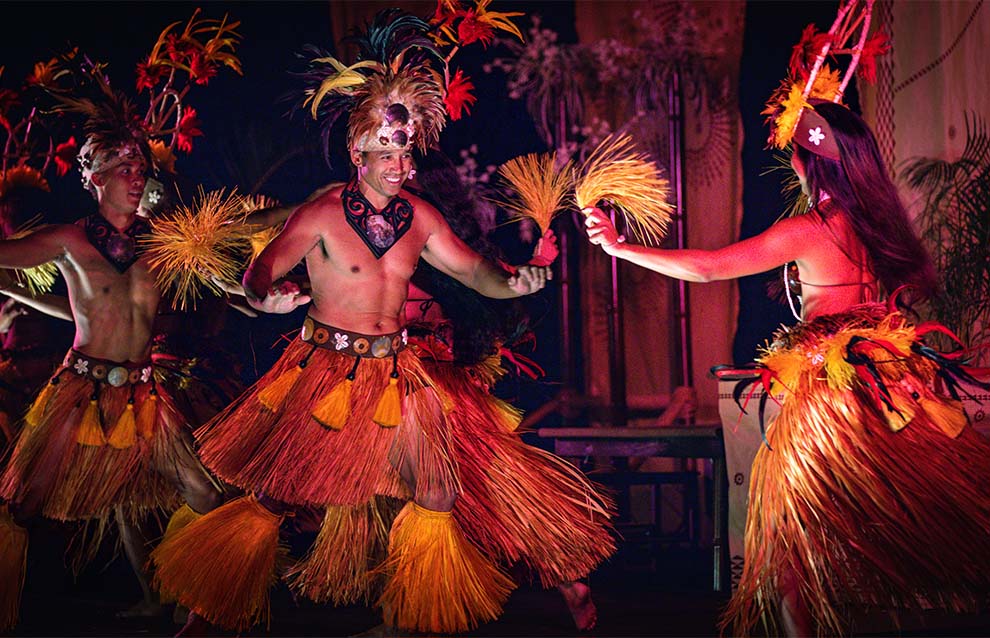 Dancers in traditional costumes perform energetically with grass skirts and feathered accessories.