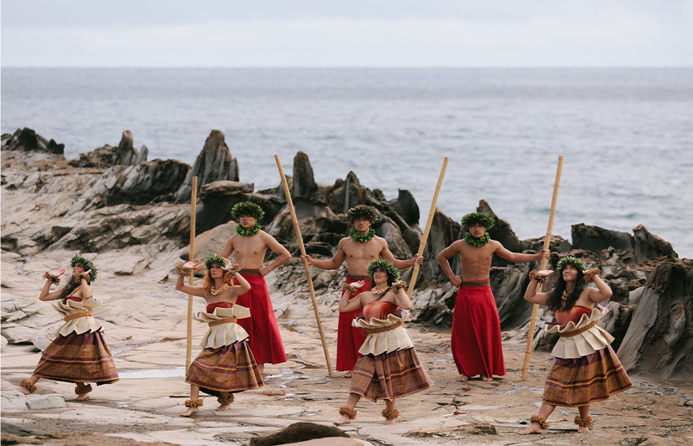 Dancers in traditional costumes perform energetically with grass skirts and feathered accessories.