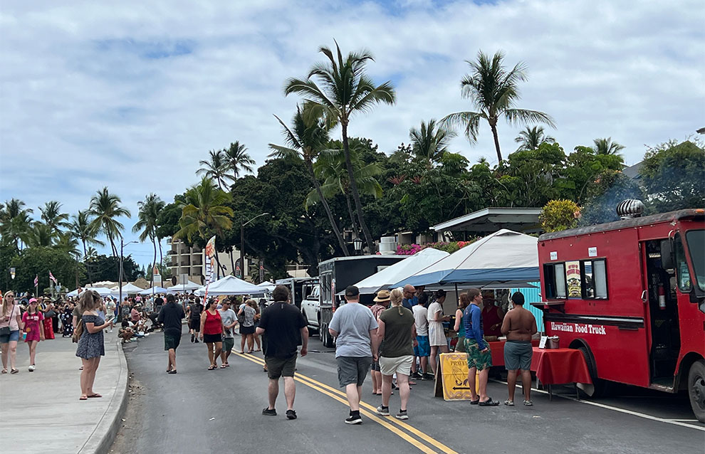 a street full of people walking along a line of food trucks